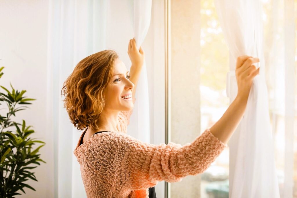 Beautiful woman opening curtains at home